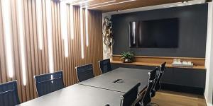 Na sala de reunião, o ripado de lâmina Leblon se estende da parede ao teto, com uma iluminação personalizada